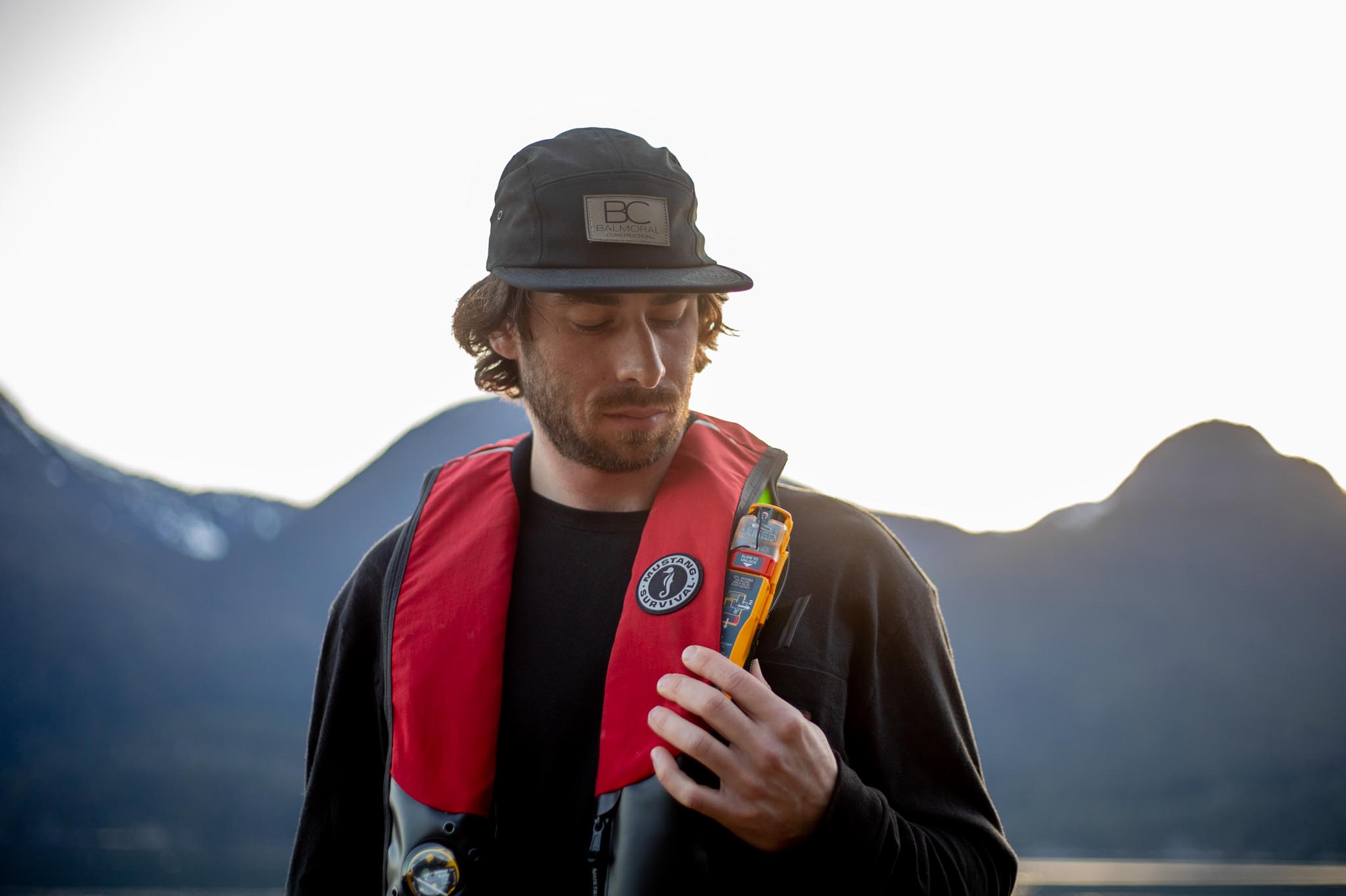 Sailor wearing a red Mustang lifejacket with rescueME PLB3 beside a mountain lake