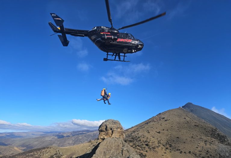 Georgia and a rescue paramedic being winched beneath a helicopter above the Mount Difficulty ridgeline
