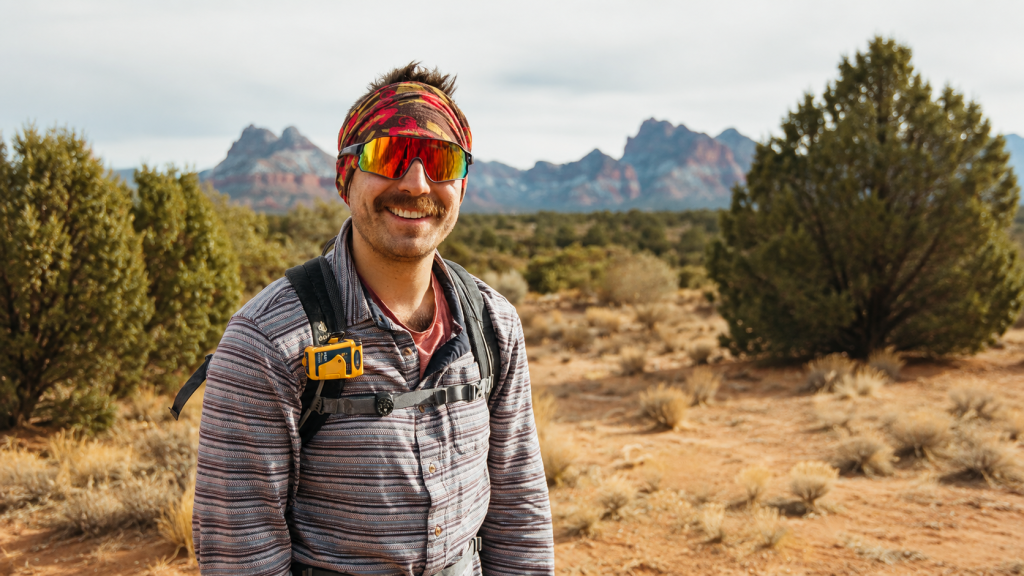Hiker carrying an Ocean Signal rescueME PLB1 clipped visibly to a backpack shoulder strap in remote terrain