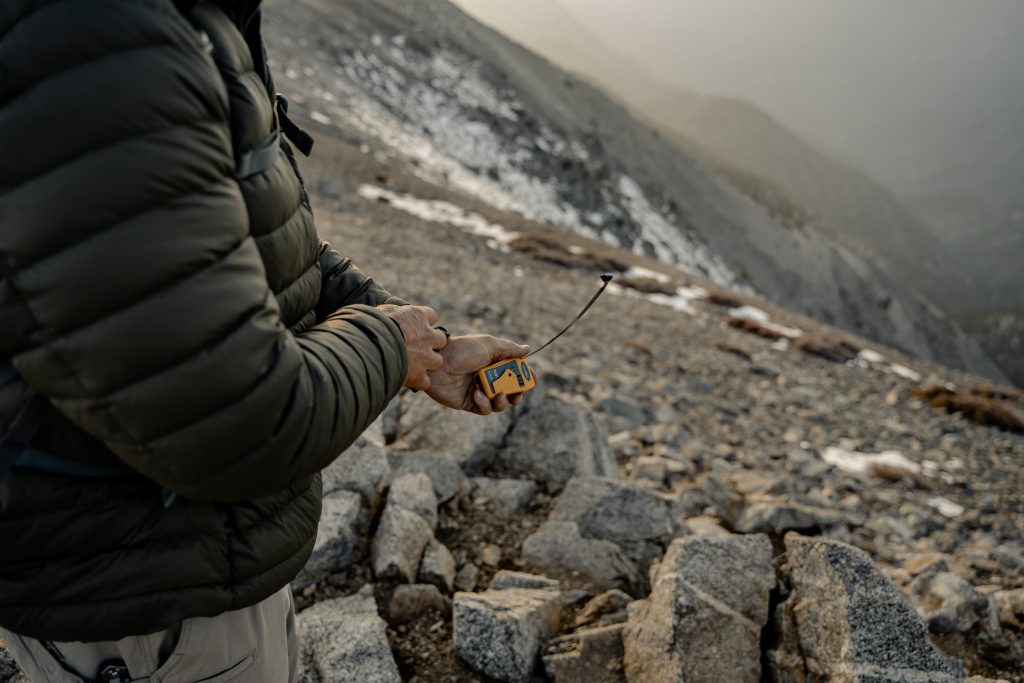 Hiker holding an Ocean Signal rescueME PLB1 with its antenna fully extended in mountain terrain