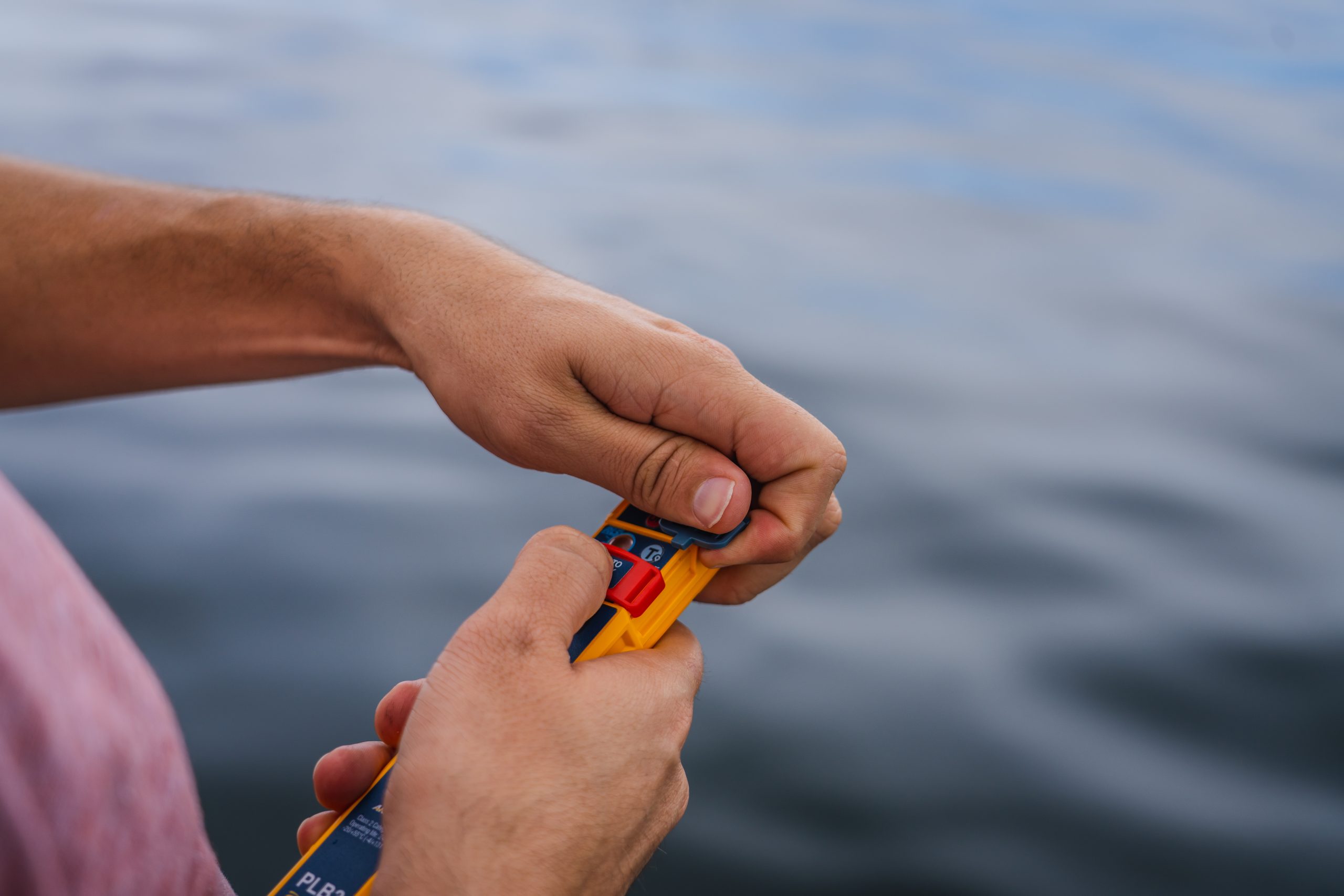 Hands operating the arming and activation slides on an Ocean Signal rescueME PLB3