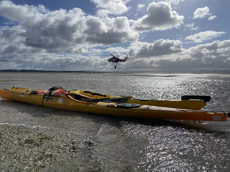 Ambulance helicopter carrying out a winch rescue beyond two sea kayaks on a sandbank at Wilsons Promontory